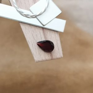 The dark red garnet teardrop displayed on a jewellers bench peg with some sterling silver sheet and wire.