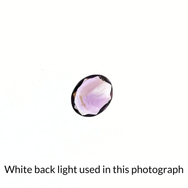 The purple amethyst oval gem is being back-lit with a bright white light to show any inclusions within the gem more clearly.