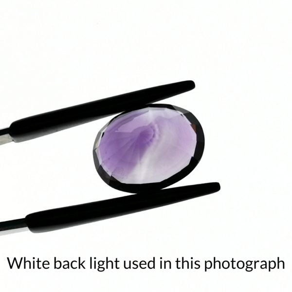 The purple amethyst oval gem is being back-lit with a bright white light to show any inclusions within the gem more clearly.