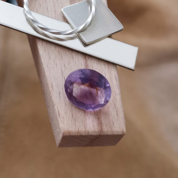 The purple amethyst oval displayed on a jewellers bench peg with some sterling silver sheet and wire.
