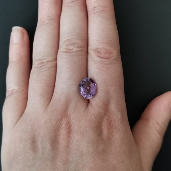 The purple amethyst gem resting on a hand to give an idea of the gemstone size and colour.