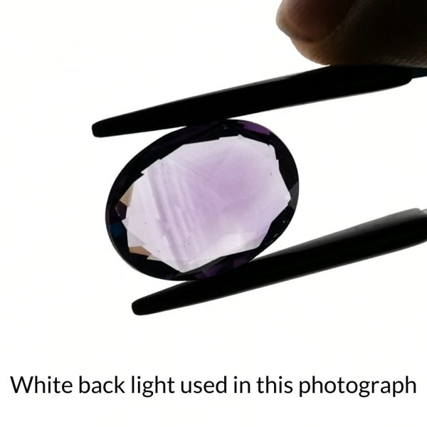 The purple amethyst oval gem is being back-lit with a bright white light to show any inclusions within the gem more clearly.