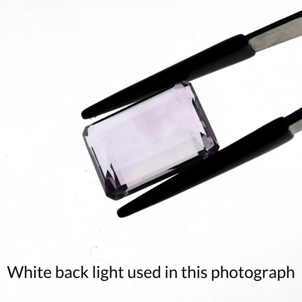 The purple amethyst rectangle gem is being back-lit with a bright white light to show any inclusions within the gem more clearly.