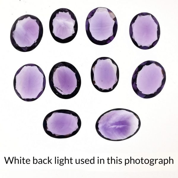 The purple amethyst oval gems are being back-lit with a bright white light to show any inclusions within the gem more clearly.