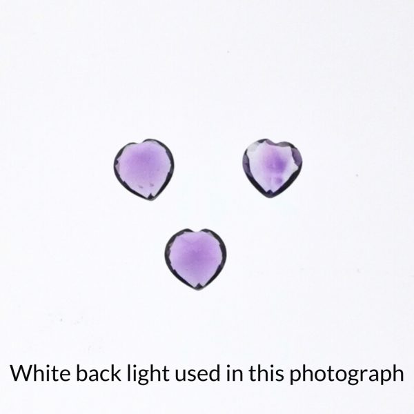 The purple amethyst heart gems are being back-lit with a bright white light to show any inclusions within the gems more clearly.