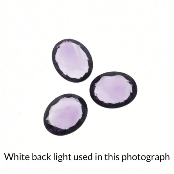 The purple amethyst oval gems is being back-lit with a bright white light to show any inclusions within the gem more clearly.