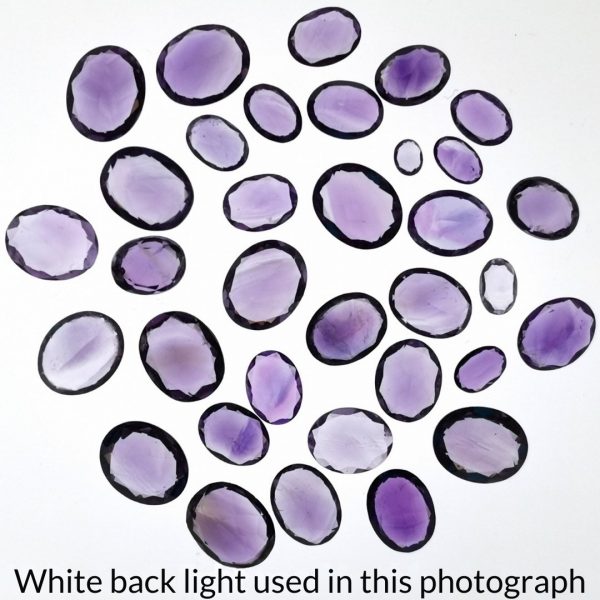 The bundle of purple amethyst oval gems are being back-lit with a bright white light to show any inclusions within the gem more clearly.