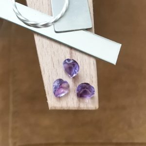 The purple amethyst hearts displayed on a jewellers bench peg with some sterling silver sheet and wire.