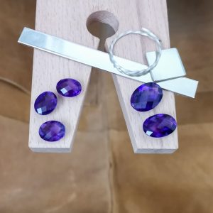 The bundle of purple amethyst ovals displayed on a jewellers bench peg with some sterling silver sheet and wire.