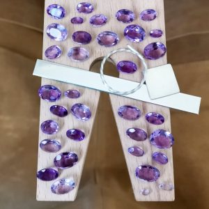 The large bundle of purple amethyst ovals displayed on a jewellers bench peg with some sterling silver sheet and wire.