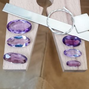 The elongated purple amethyst ovals displayed on a jewellers bench peg with some sterling silver sheet and wire.