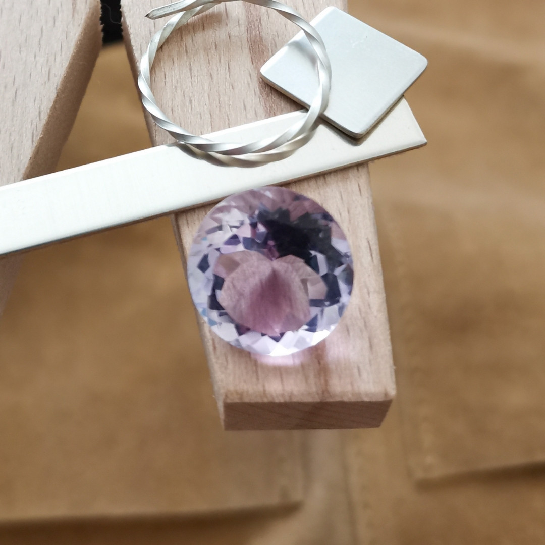 The purple amethyst round displayed on a jewellers bench peg with some sterling silver sheet and wire.