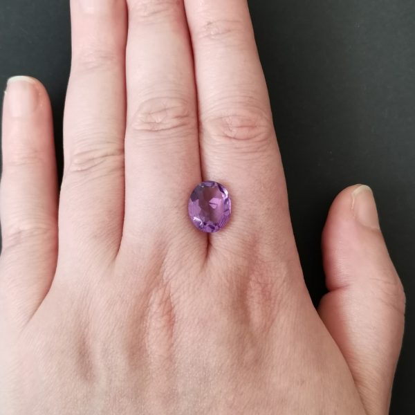 The purple amethyst gemstone resting on a hand to give an idea of the gemstone size and colour.