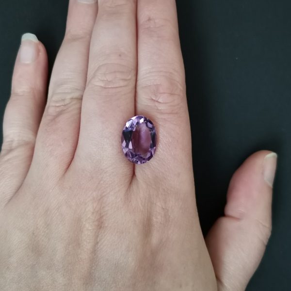 The purple amethyst gemstone resting on a hand to give an idea of the gemstone size and colour.