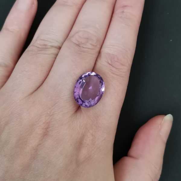 The purple amethyst gemstone resting on a hand to give an idea of the gemstones size and colour.