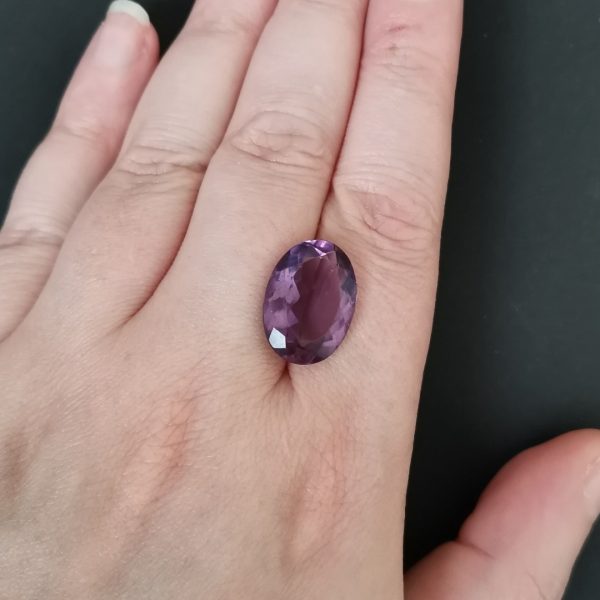 The purple amethyst gemstone resting on a hand to give an idea of the gemstones size and colour.