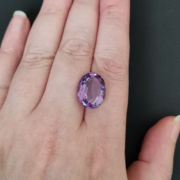 The purple amethyst gemstone resting on a hand to give an idea of the gemstones size and colour.