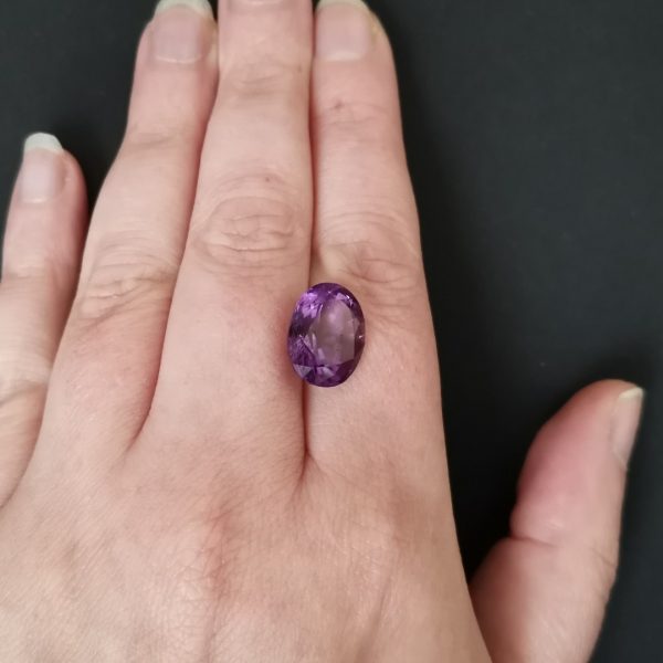 The purple amethyst gemstone resting on a hand to give an idea of the gemstone size and colour.