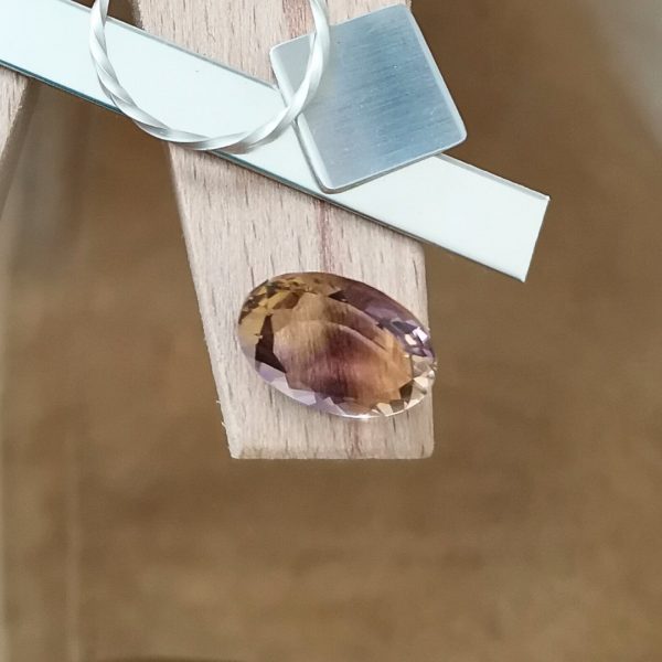 The purple and yellow ametrine oval displayed on a jewellers bench peg with some sterling silver sheet and wire.