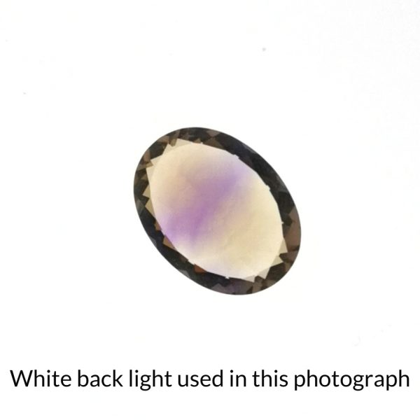 The purple and yellow ametrine oval gem is being back-lit with a bright white light to show any inclusions within the gem more clearly.