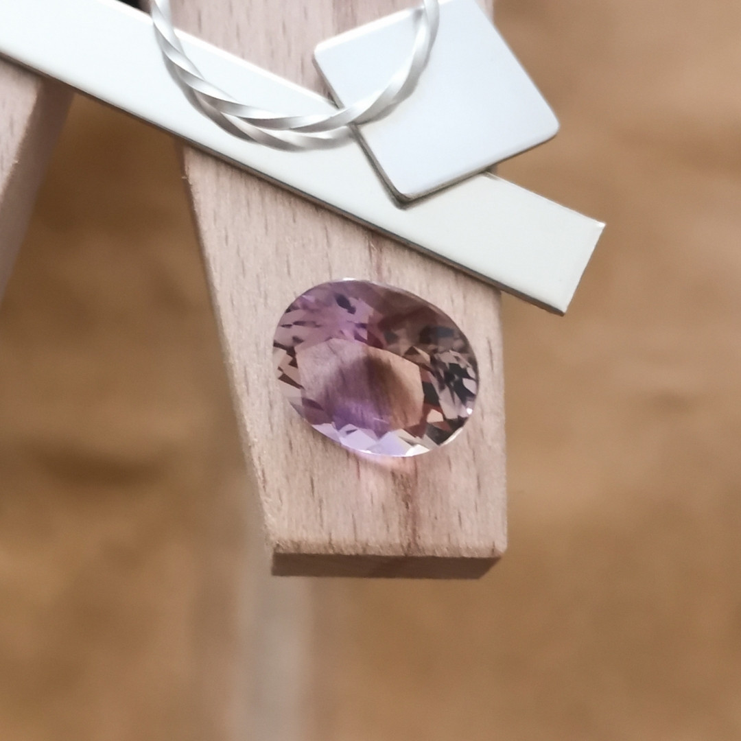 The purple and yellow ametrine oval displayed on a jewellers bench peg with some sterling silver sheet and wire.