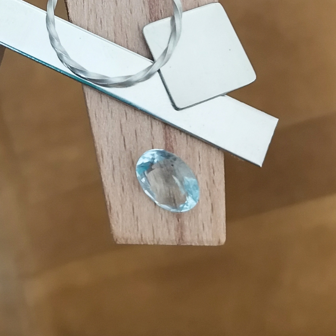The blue aquamarine oval displayed on a jewellers bench peg with some sterling silver sheet and wire.