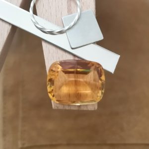 The cushion cut orange citrine displayed on a jewellers bench peg with some sterling silver sheet and wire.