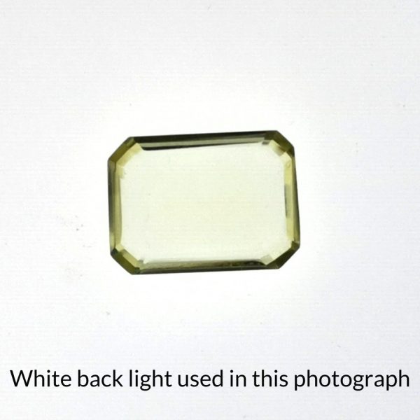 The yellow citrine rectangle gem is being back-lit with a bright white light to show any inclusions within the gem more clearly.