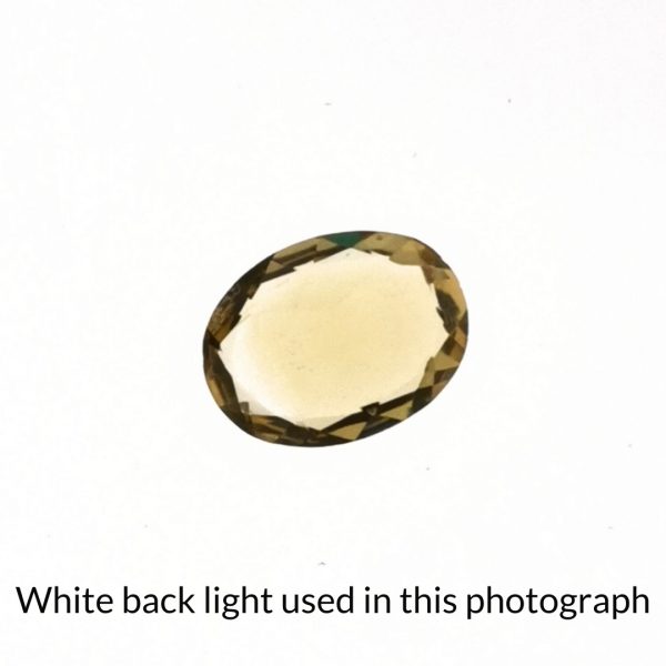 The yellow citrine oval gem is being back-lit with a bright white light to show any inclusions within the gem more clearly.
