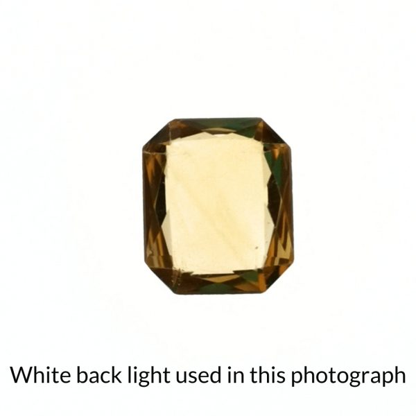 The orangy yellow citrine rectangle gem is being back-lit with a bright white light to show any inclusions within the gem more clearly.