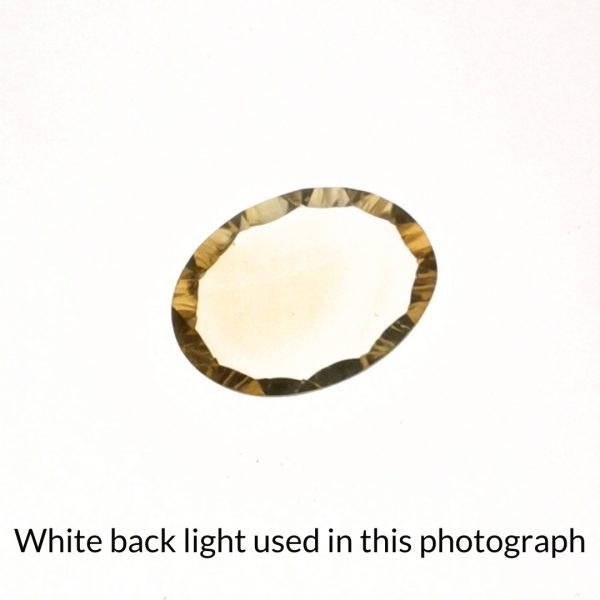 The golden citrine oval gem is being back-lit with a bright white light to show any inclusions within the gem more clearly.