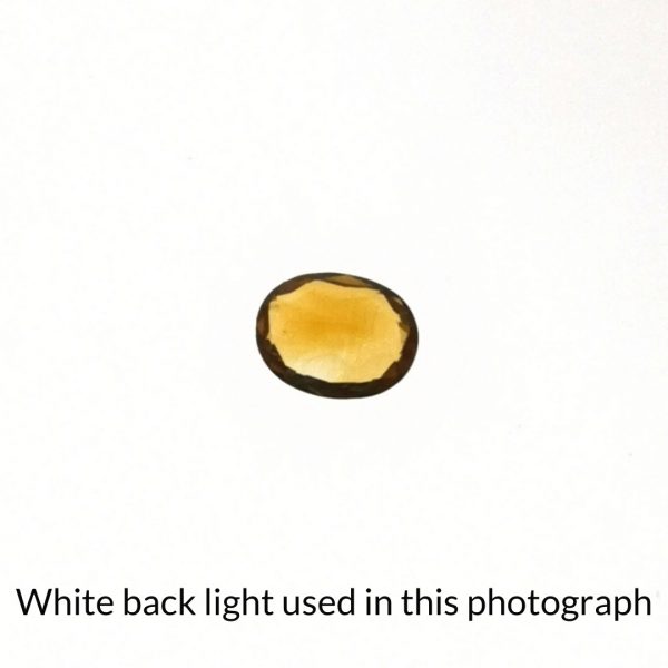 The orange citrine oval gem is being back-lit with a bright white light to show any inclusions within the gem more clearly.