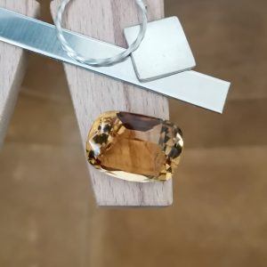 The yellow citrine with it's cushion cut displayed on a jewellers bench peg with some sterling silver sheet and wire.