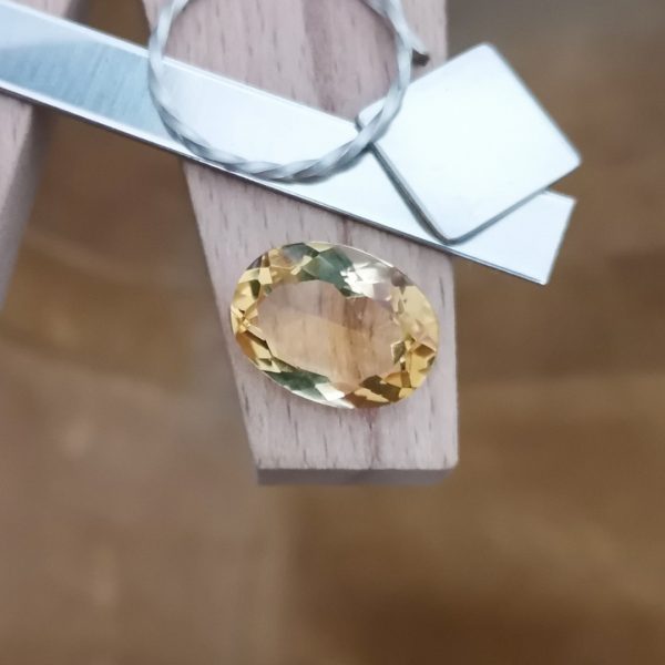 The golden yellow citrine oval displayed on a jewellers bench peg with some sterling silver sheet and wire.