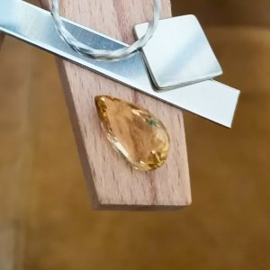The golden yellow citrine teardrop displayed on a jewellers bench peg with some sterling silver sheet and wire.