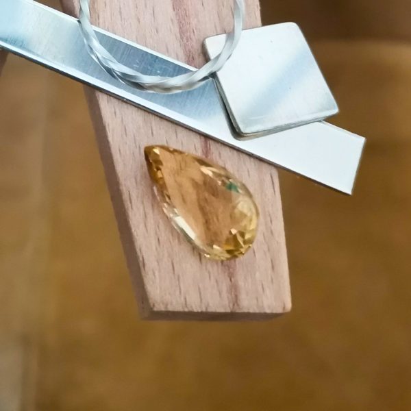 The golden yellow citrine teardrop displayed on a jewellers bench peg with some sterling silver sheet and wire.