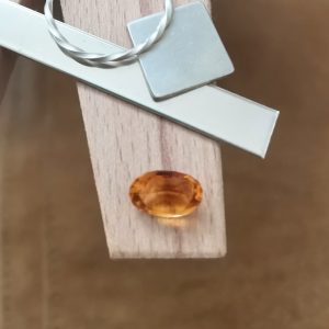 The orange citrine oval displayed on a jewellers bench peg with some sterling silver sheet and wire.