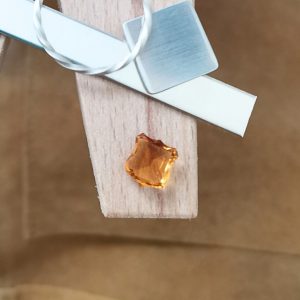 The fancy orange citrine displayed on a jewellers bench peg with some sterling silver sheet and wire.