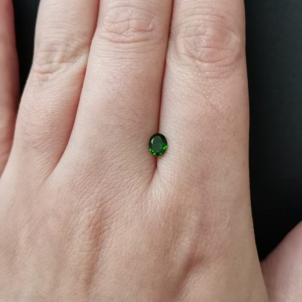 The green diopside gemstone resting on a hand to give an idea of the gemstone size and colour.