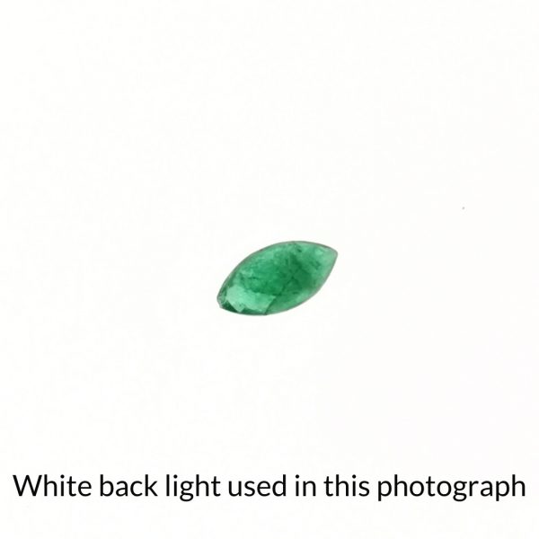 The green emerald marquise gem is being back-lit with a bright white light to show any inclusions within the gem more clearly.