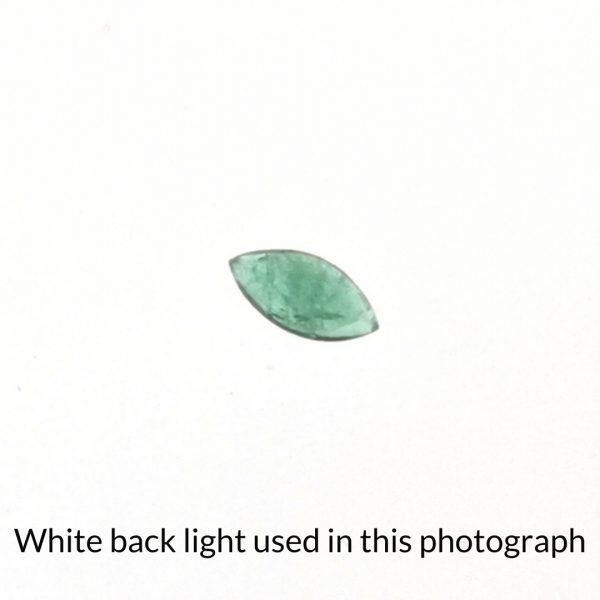 The green emerald marquise gem is being back-lit with a bright white light to show any inclusions within the gem more clearly.