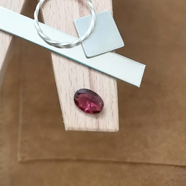 The pink garnet oval displayed on a jewellers bench peg with some sterling silver sheet and wire.
