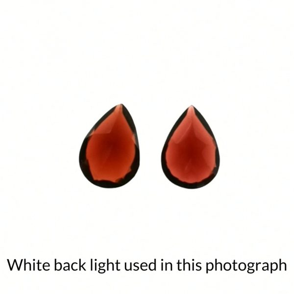 The pair of red garnet teardrop gems are being back-lit with a bright white light to show any inclusions within the gem more clearly.