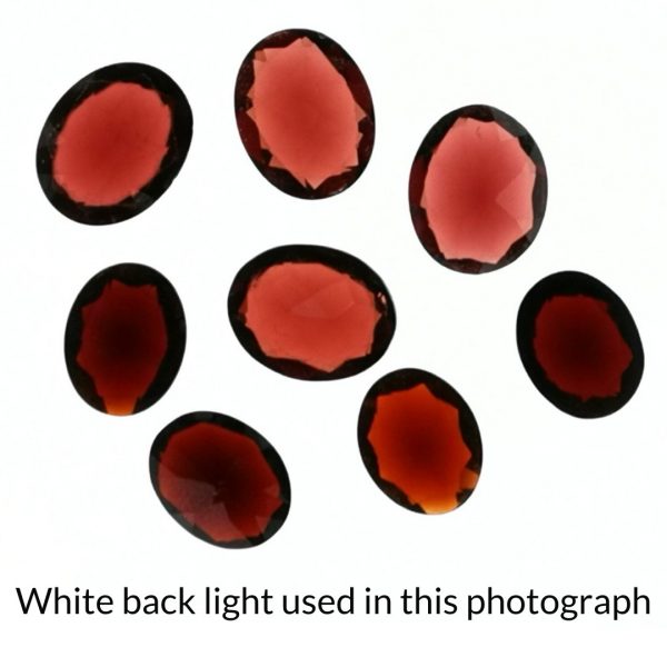 The red garnet oval gems is being back-lit with a bright white light to show any inclusions within the gems more clearly.
