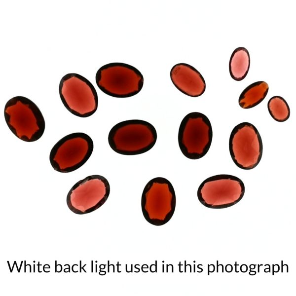 The red garnet oval gems is being back-lit with a bright white light to show any inclusions within the gem more clearly.