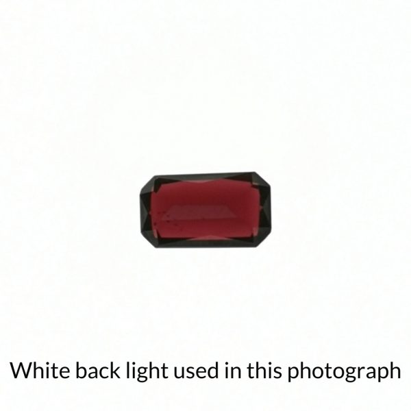 The red garnet rectangle gem is being back-lit with a bright white light to show any inclusions within the gem more clearly.
