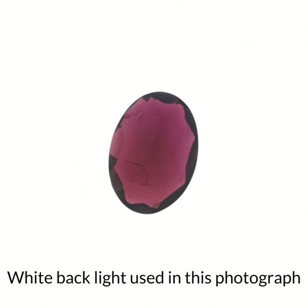 The red garnet oval gem is being back-lit with a bright white light to show any inclusions within the gem more clearly.