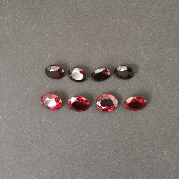 All 8 of the red garnet ovals shown on a black background. 4 are in darker shades, and 4 are in brighter shades.