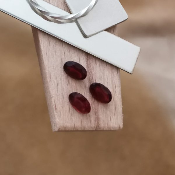 The red garnet ovals displayed on a jewellers bench peg with some sterling silver sheet and wire.