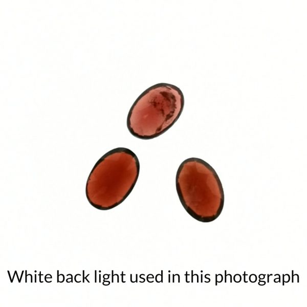 The red garnet oval gems is being back-lit with a bright white light to show any inclusions within the gems more clearly.